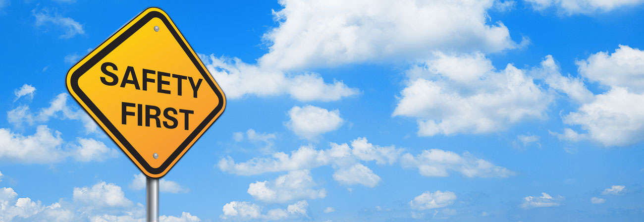 A yellow traffic sign reading Safety First in front of a blue sky with fluffy clouds.