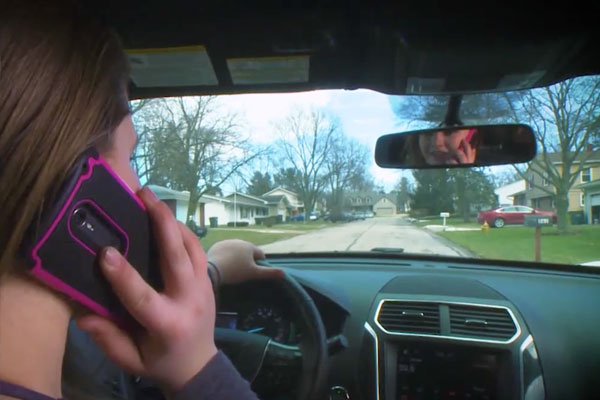 backseat view of a girl driving while on her cell phone