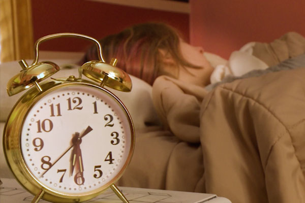 someone sleeping in a bed with an old fashioned alarm clock in the foreground