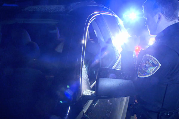 a stopped car with a police officer shining a light through the window