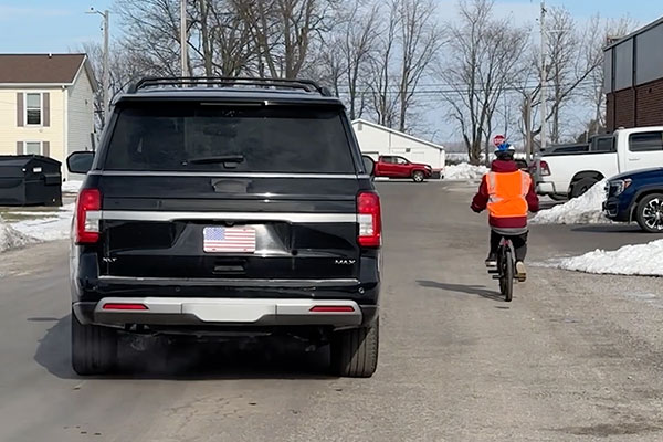 back of an suv next to a cyclist on the road with enough room between them