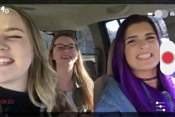 three teens in a car singing and recording while driving